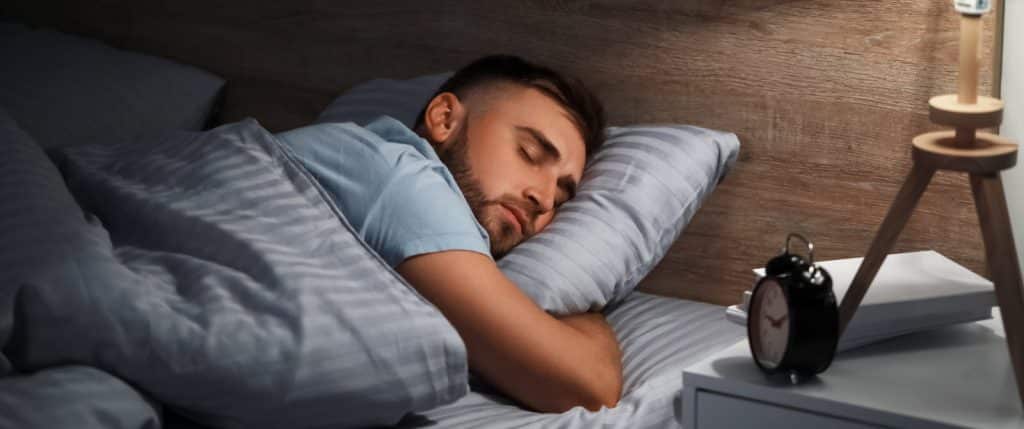 Homme dormant paisiblement dans son lit, le sommeil étant l'un des bénéfices d'une activité physique régulière