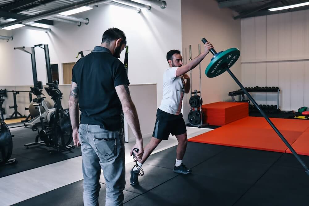 Exercice de rotation avec une barre en appui au sol, encadré par un coach pendant une séance de préparation physique
