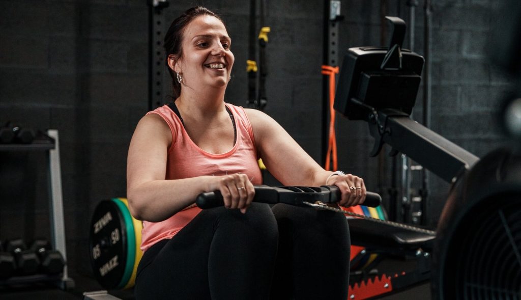 Cliente souriante pendant une séance de rameur chez Ultimate Physical