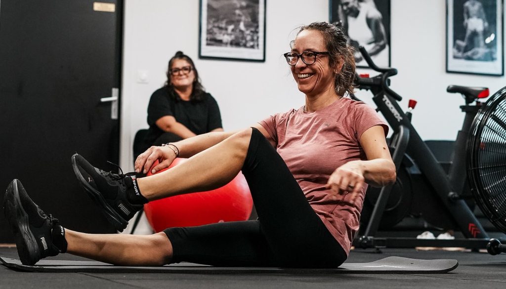Mal de dos au bureau : une cliente assise sur un tapis fait un exercice de mobilité du tronc, encadrée dans un centre Ultimate Physical