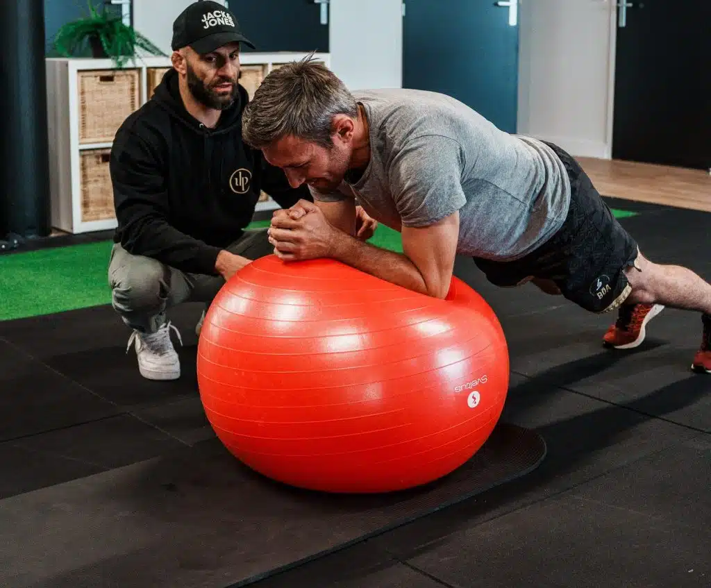 Sport sur ordonnance à Bordeaux et Mérignac 3 Coach Ultimate qui encadre de près un exercice de gainage sur ballon, séance d'activité physique adaptée