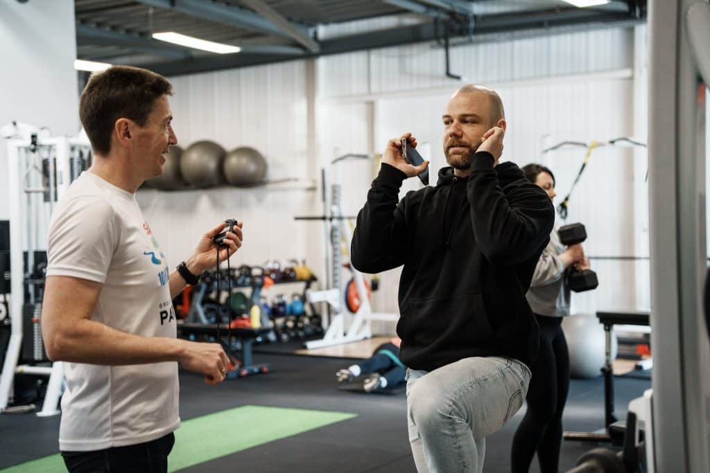 Test de mouvement pendant un bilan sportif personnalisé : un coach chronomètre un client qui réalise une fente
