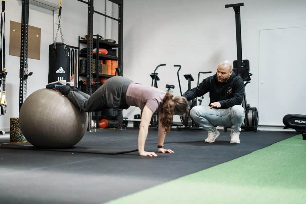 Coach sportif Eysines et Le Haillan : un coach d'Ultimate Physical corrige la position d'une cliente en gainage sur un swiss ball