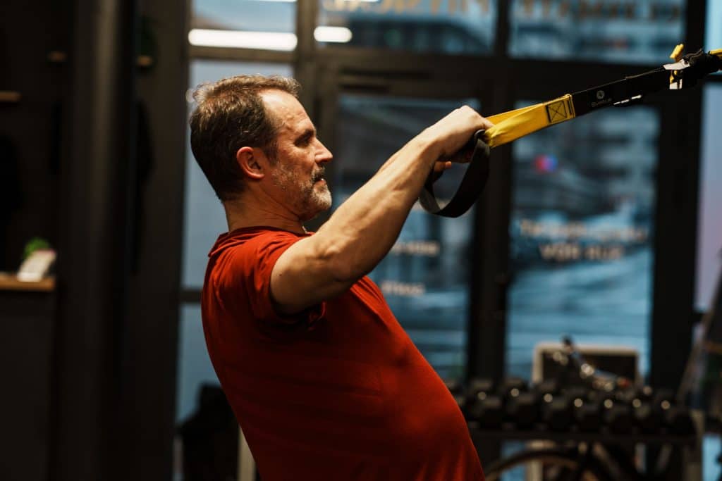 Homme d'une soixantaine d'années en renforcement musculaire au TRX pour lutter contre la perte de masse musculaire, chez Ultimate Physical