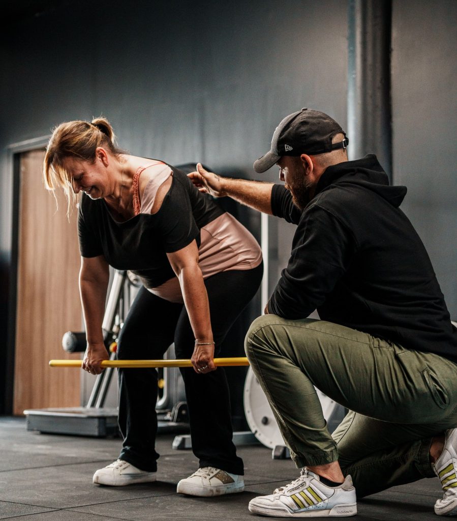 Un coach Ultimate corrige le geste d’une membre souriante pendant un exercice de renforcement