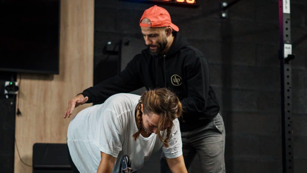 Coach sportif corrigeant la posture et le placement du dos d'une cliente pendant un exercice chez Ultimate Physical