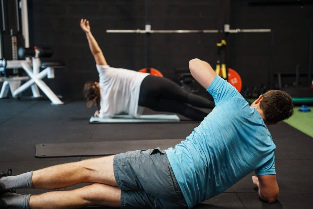 Ultimate | Le Spécialiste de l'accompagnement avec Coach sportif | Bordeaux & Mérignac 12 Des membres réalisent des exercices de gainage et de mobilité au sol dans un centre Ultimate, limité à 6 personnes par créneau