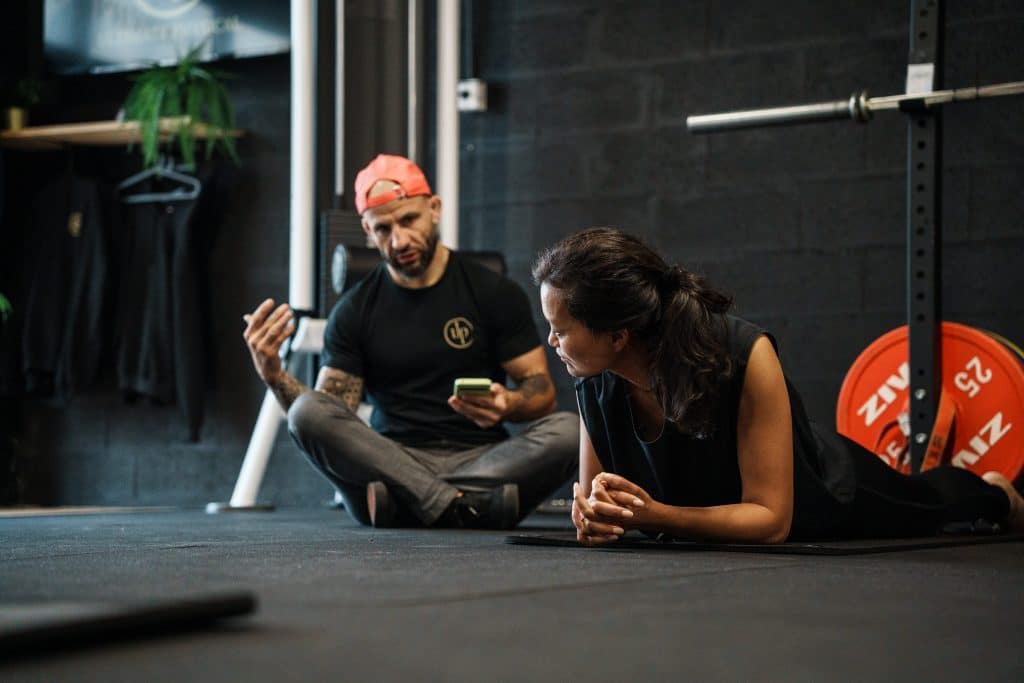 Ultimate | Le Spécialiste de l'accompagnement avec Coach sportif | Bordeaux & Mérignac 5 Un coach et une membre échangent au sol, près du matériel de musculation, dans un centre Ultimate