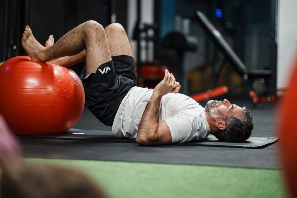 Client allongé sur un tapis, pieds sur un swiss ball, pendant une séance de récupération active contre les courbatures chez Ultimate Physical