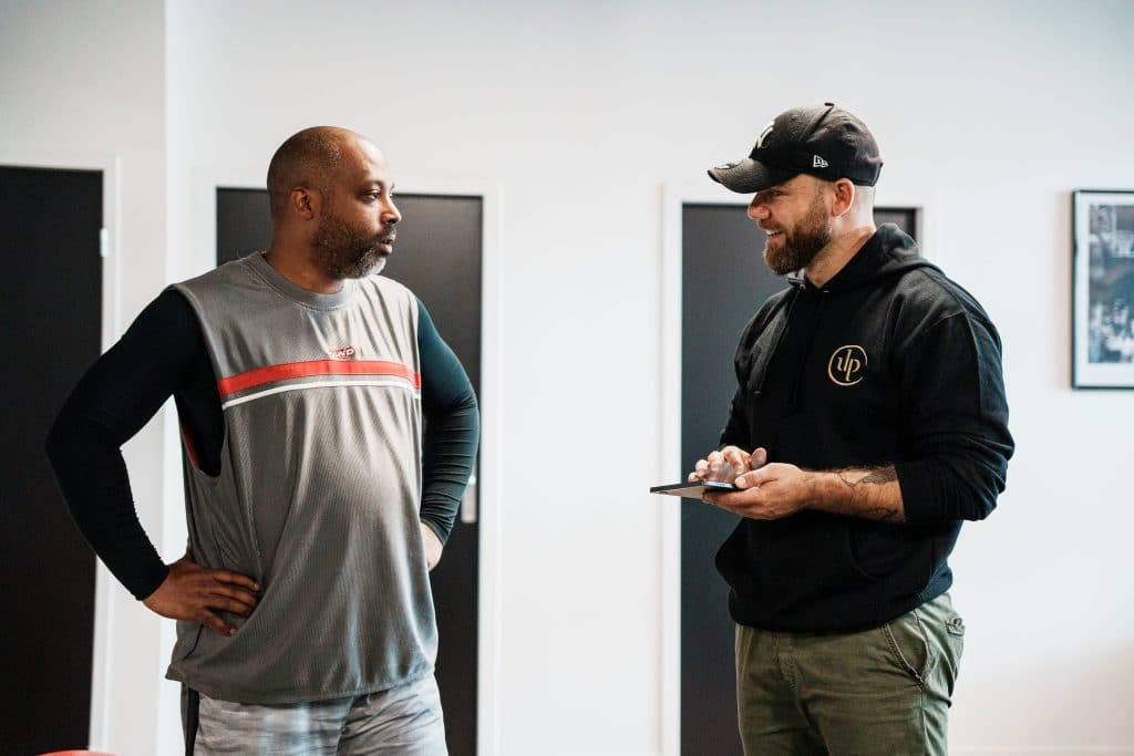 Bilan sportif personnalisé chez Ultimate Physical : un coach échange avec un client et note ses informations sur une tablette